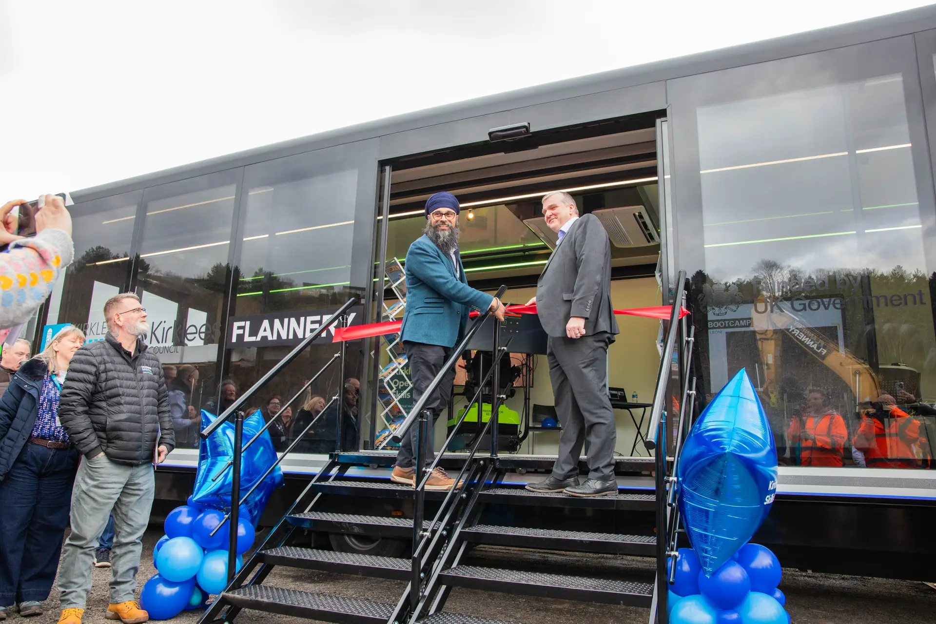 two men standing either side of a pair of scissors cutting a ribbon