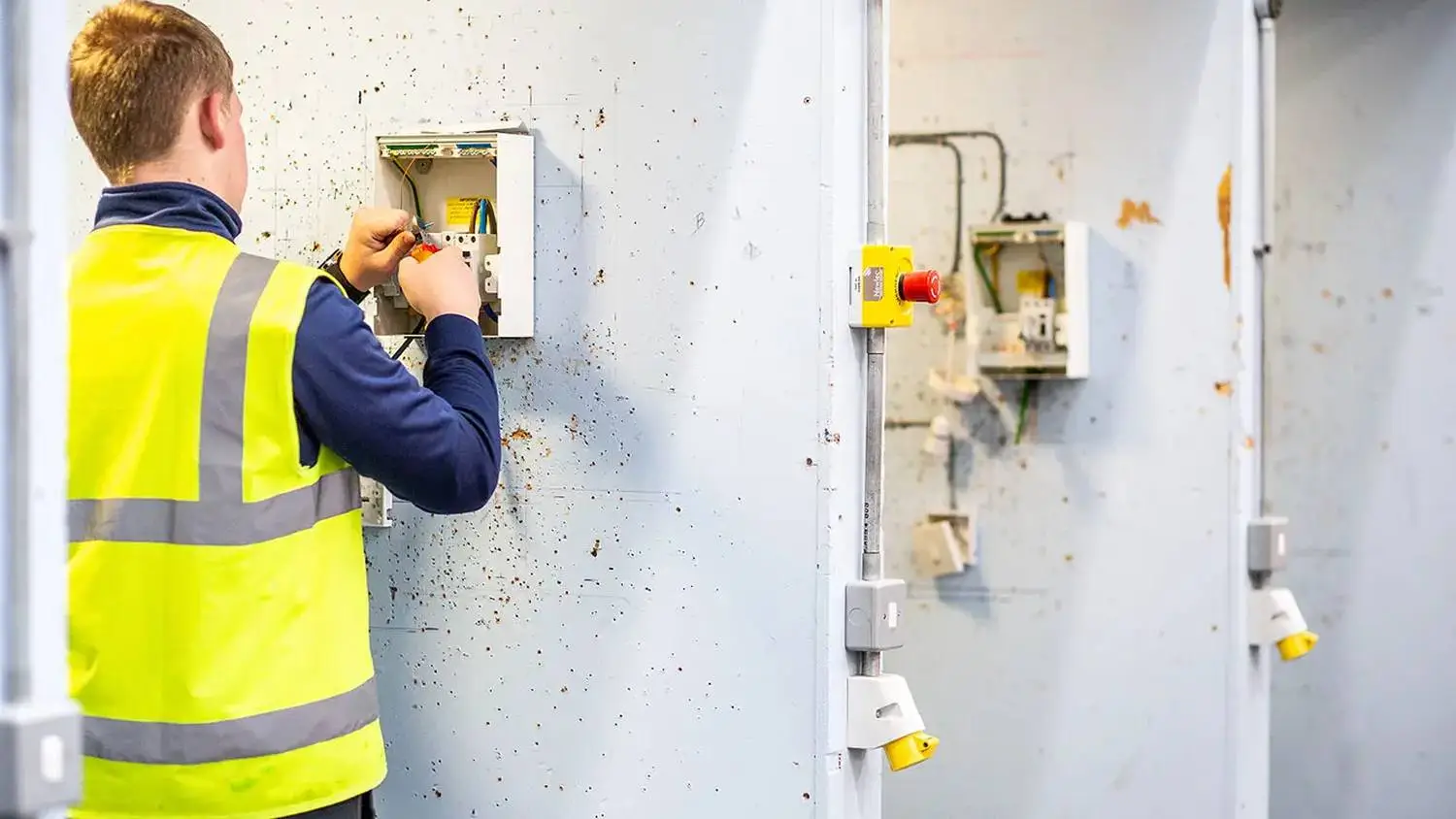 A person in a high-visibility vest working on an electrical panel with wires and switches.