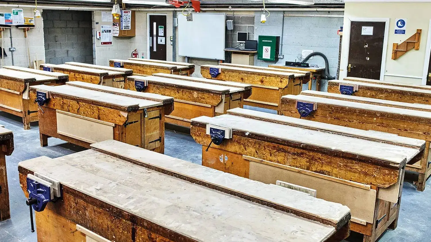 Woodworking classroom with benches, vices, and a whiteboard. Tools and equipment visible, suitable for practical carpentry lessons.