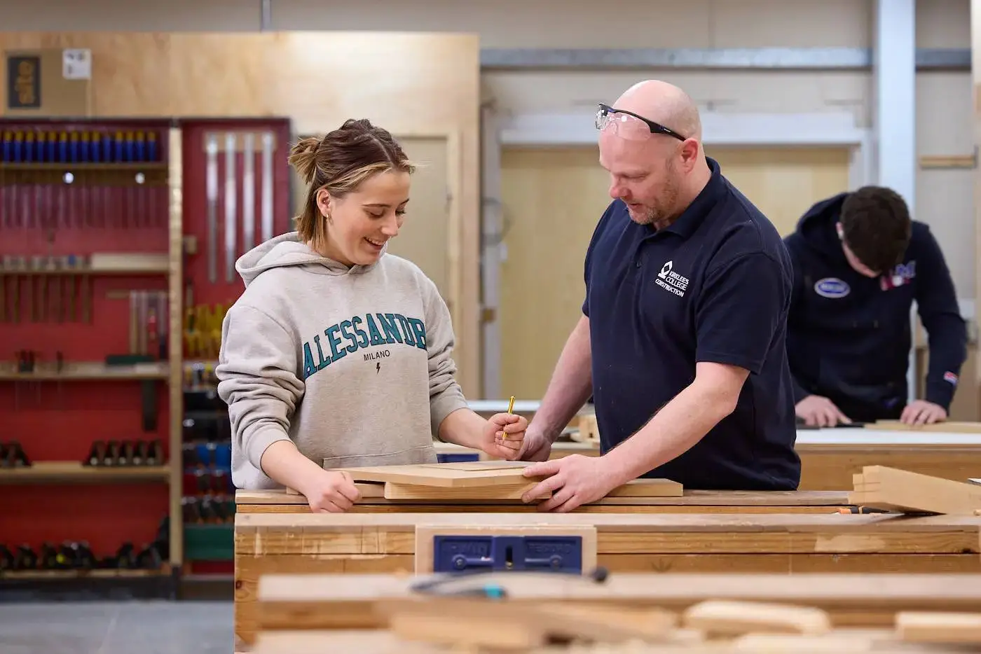 A student and teacher working on a wooden project in a well-equipped college workshop.