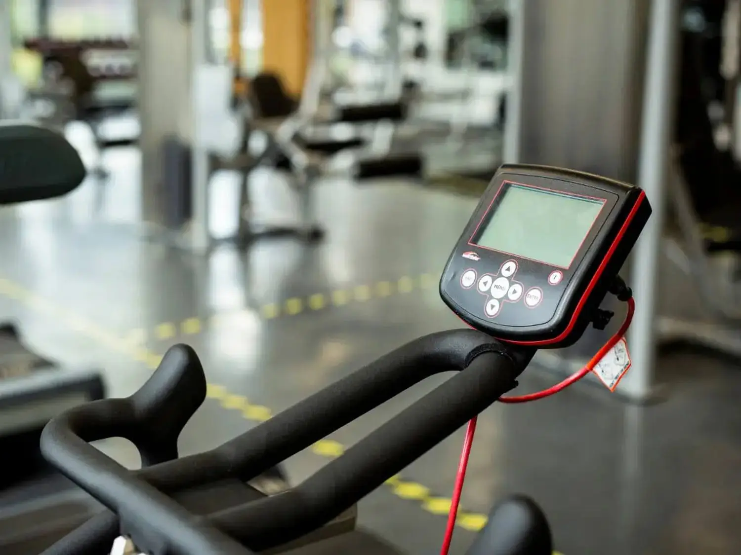 Exercise bike with digital display in a gym. Buttons include Start, Stop, and Reset. Floor marked with yellow lines.