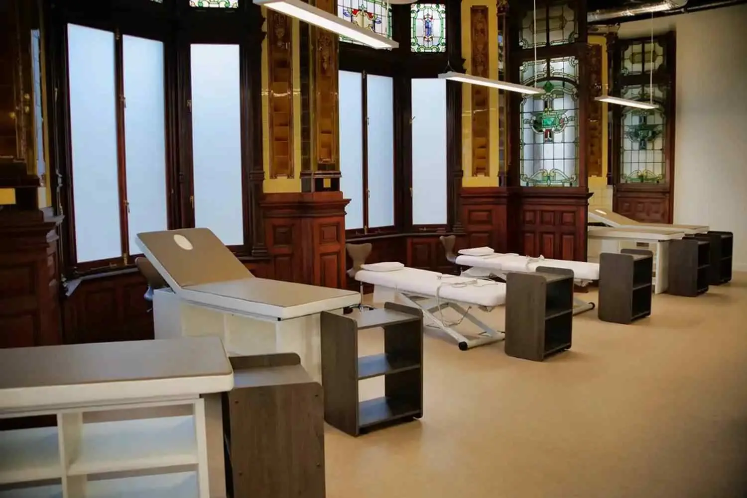 A university lecture hall with wooden panelling, stained glass windows, and adjustable desks for students.