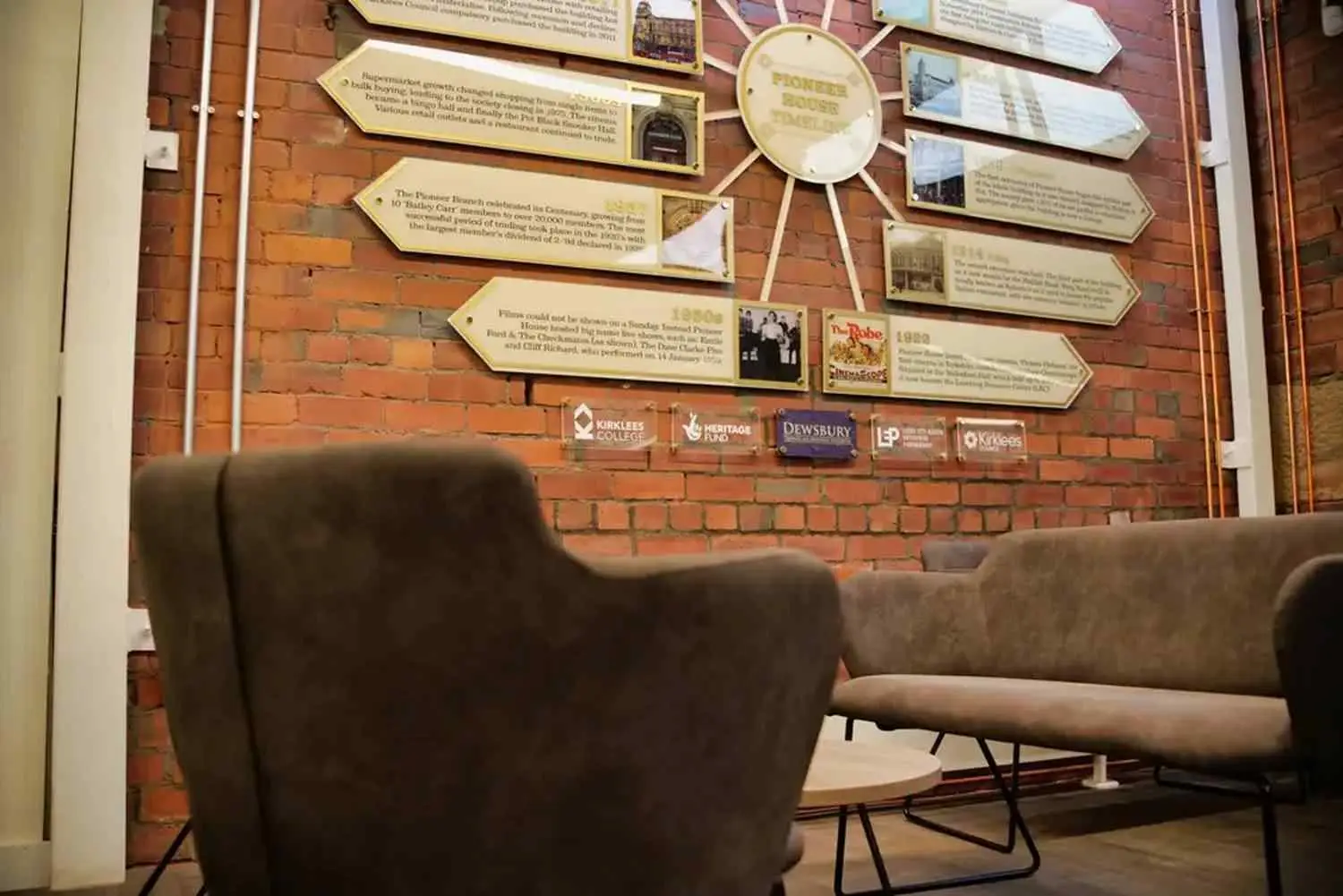 Two brown armchairs in front of a brick wall with plaques and a clock.