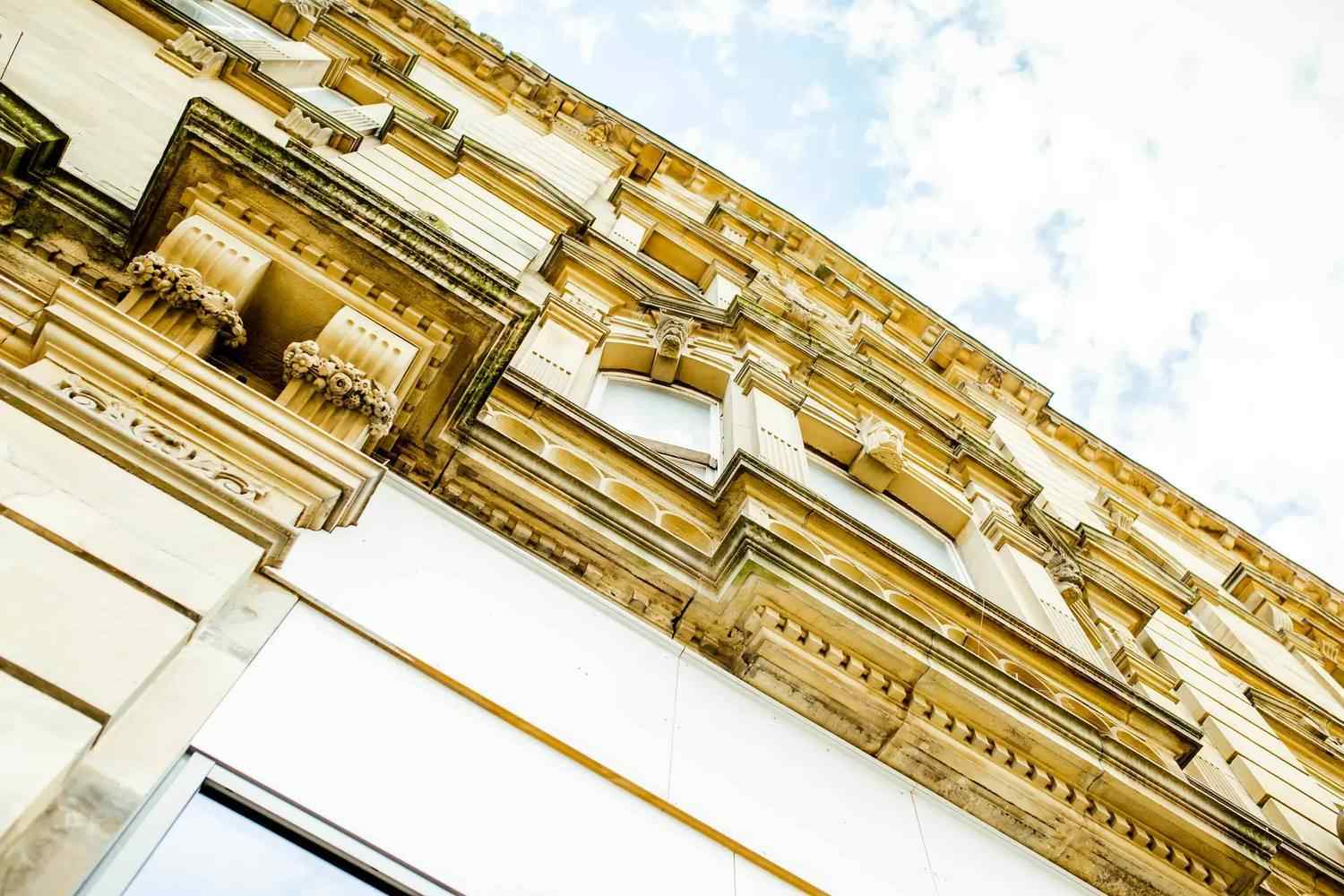A historic building facade with ornate stonework and classical architectural details under a partly cloudy sky.
