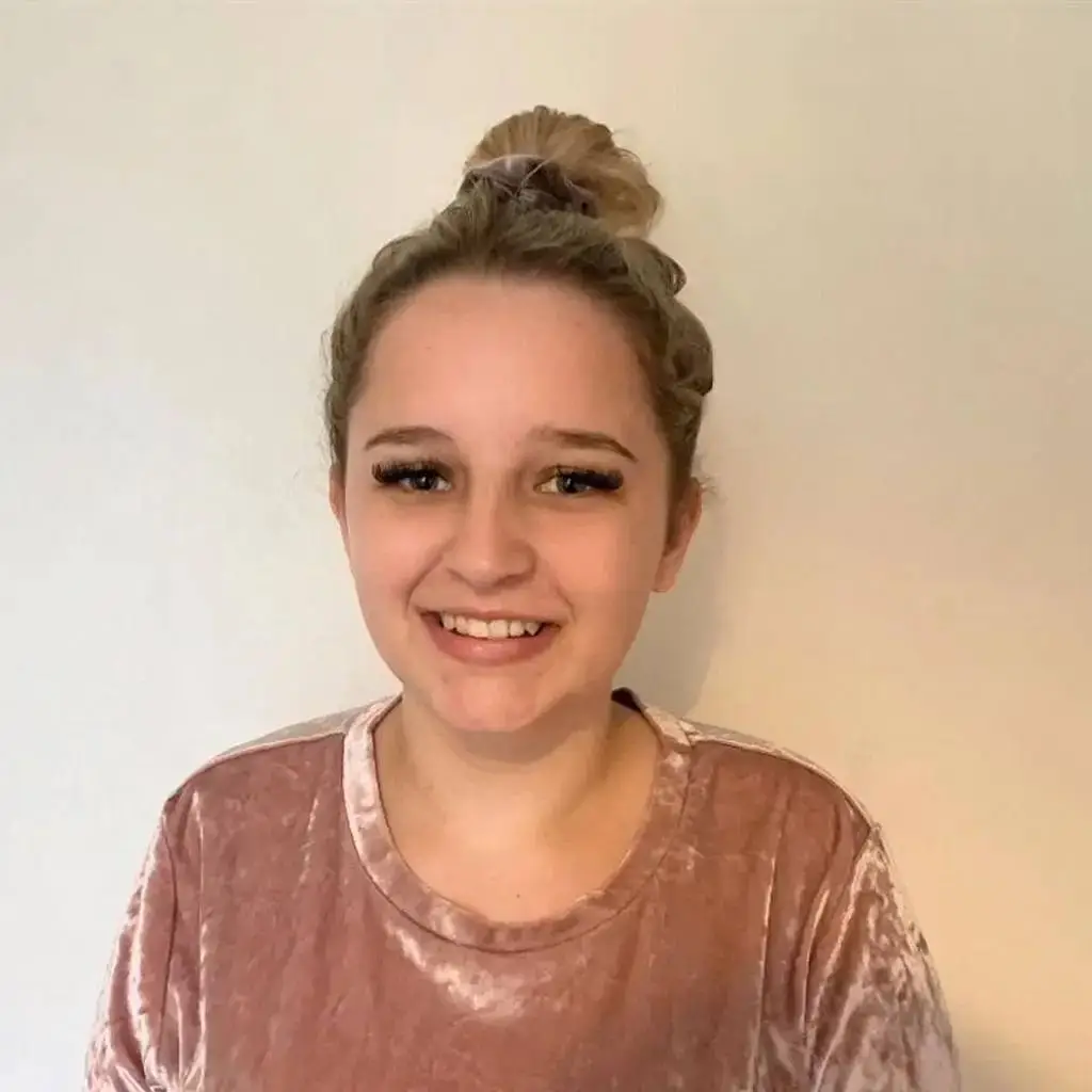 A young woman with a bun hairstyle and a pink velvet top smiles at the camera.
