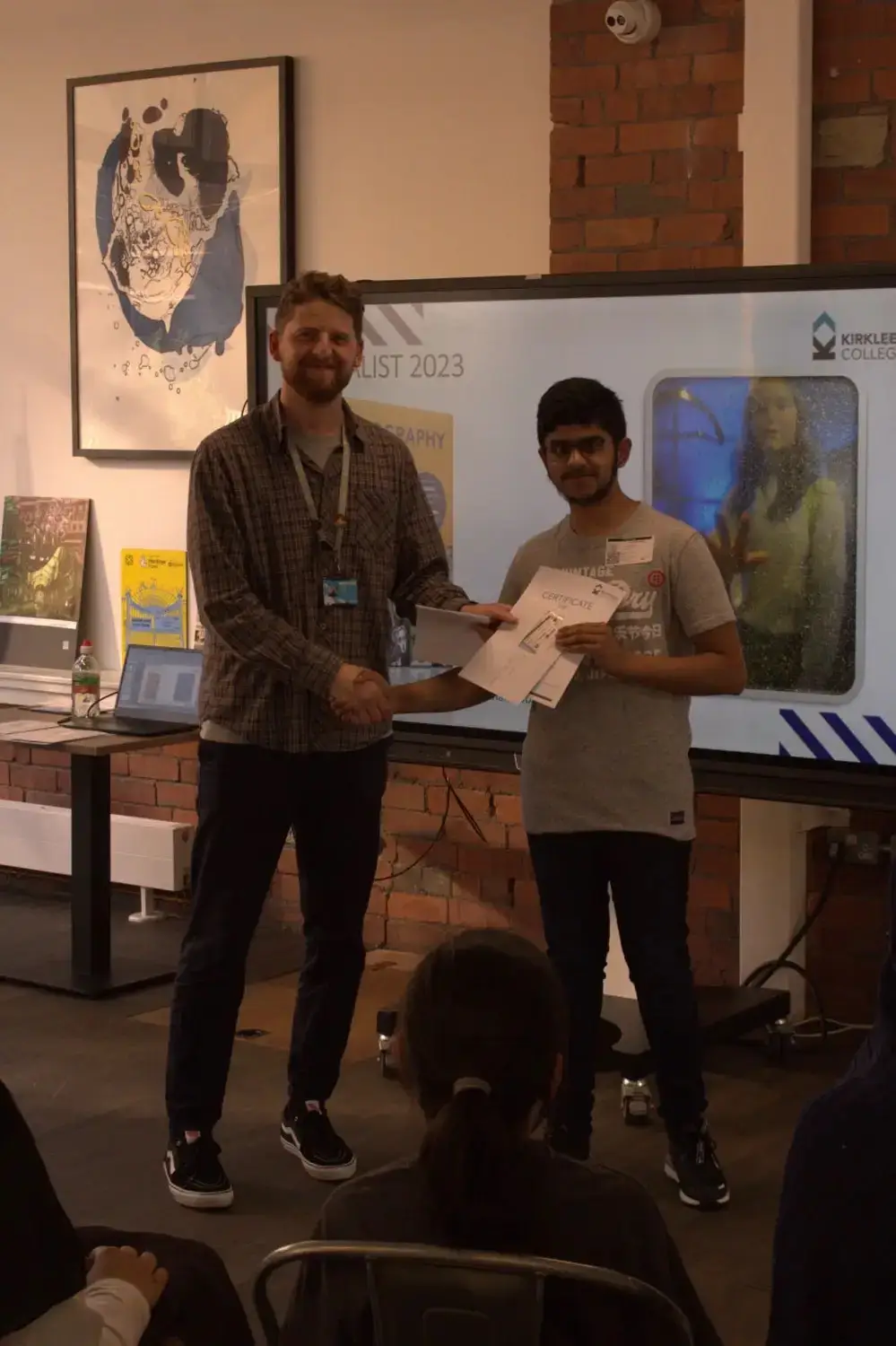 Two men shaking hands in front of a projector screen displaying Photography