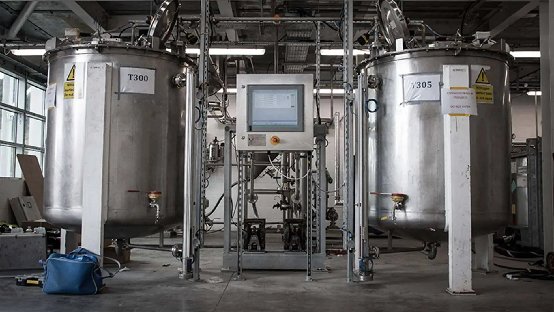 Two large stainless steel tanks with control panel in industrial setting, likely for chemical or food processing, with safety warnings and pipes.