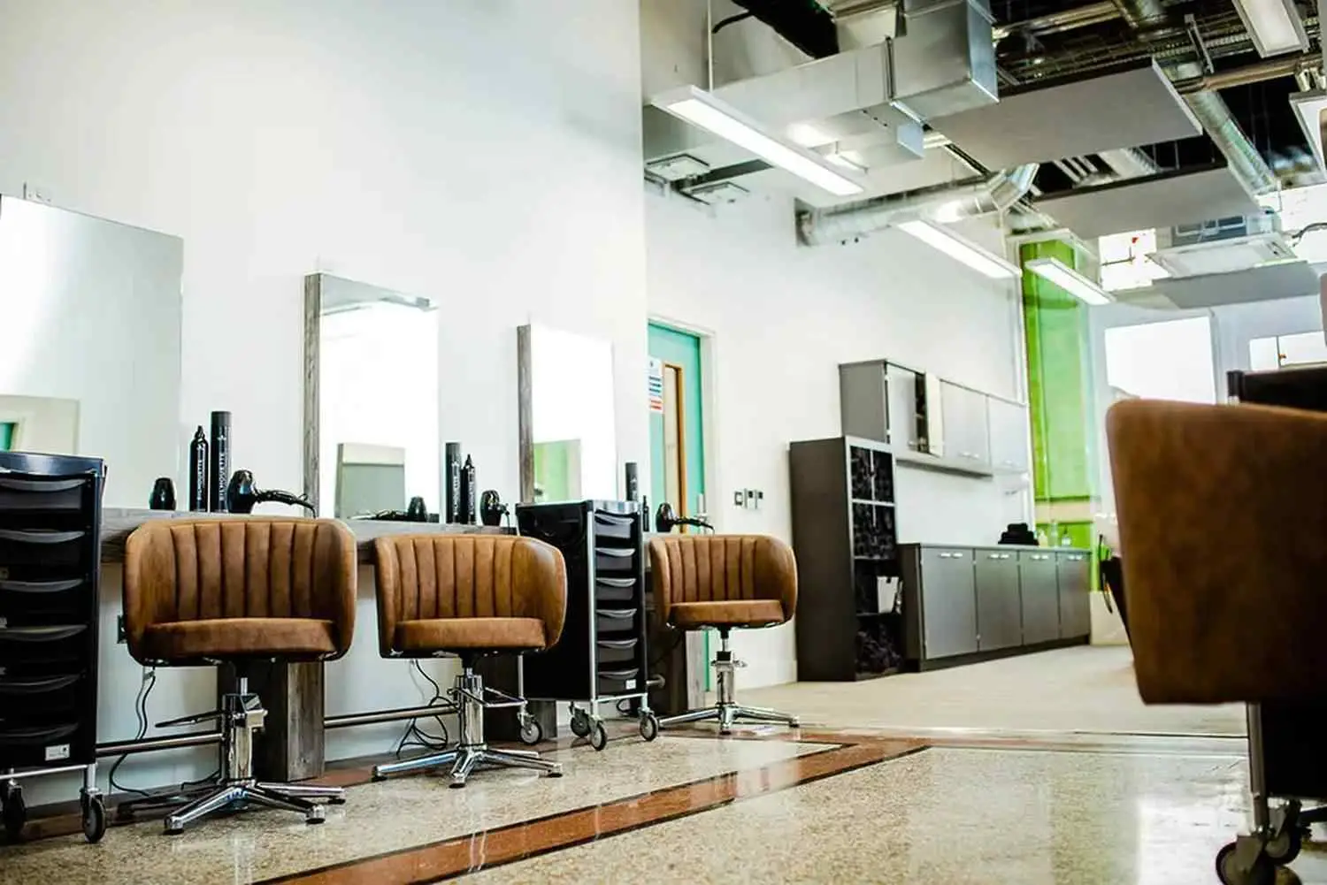 Modern hair salon with brown chairs, mirrors, and styling tools. Polished floor and industrial ceiling, ideal for a college course on hairstyling techniques.