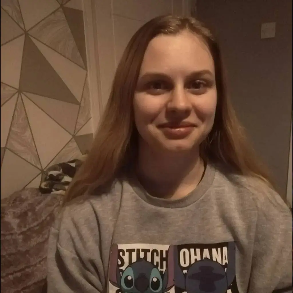 Person in grey sweatshirt with Stitch and Ohana print, smiling in front of geometric patterned wall.