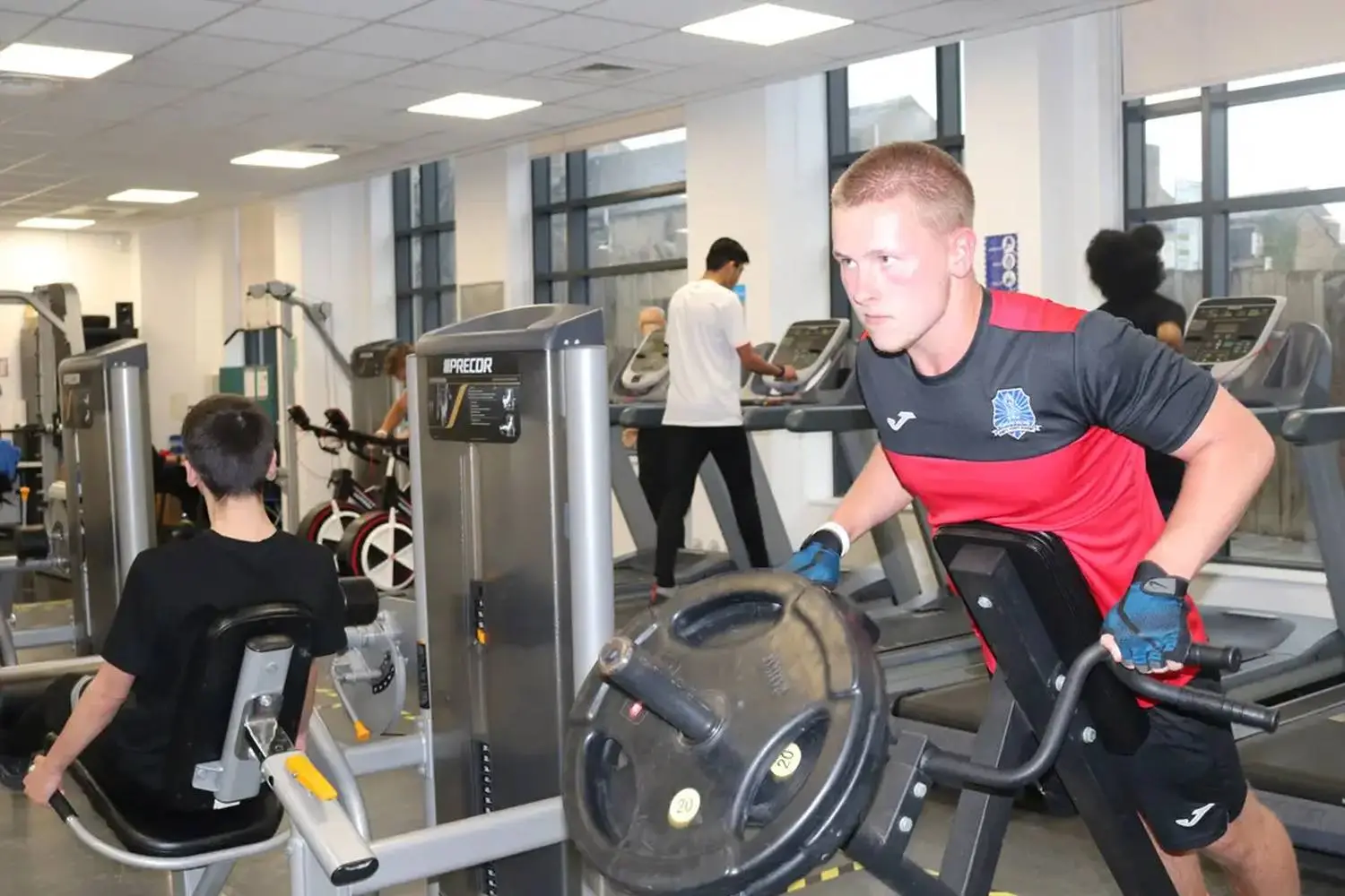 Students exercising in a college gym, using treadmills and weight machines, promoting fitness and health education.