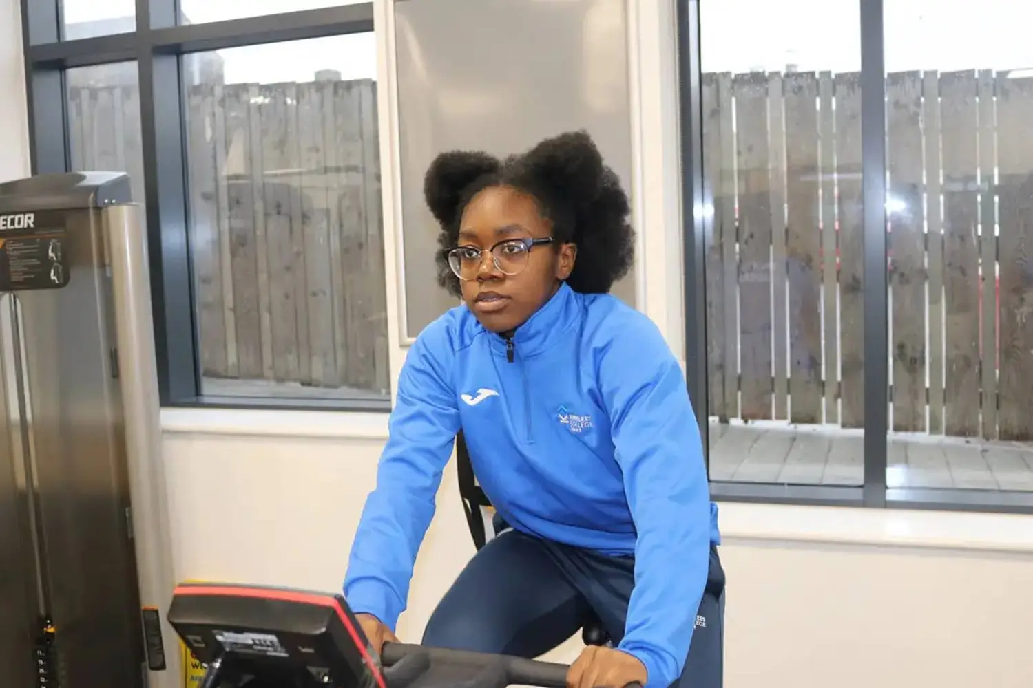 A person in a blue tracksuit cycling indoors, focused on the exercise bike's display.