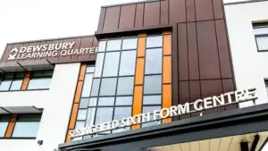 Modern college building with glass facade and signage. Students walking in front under a cloudy sky.