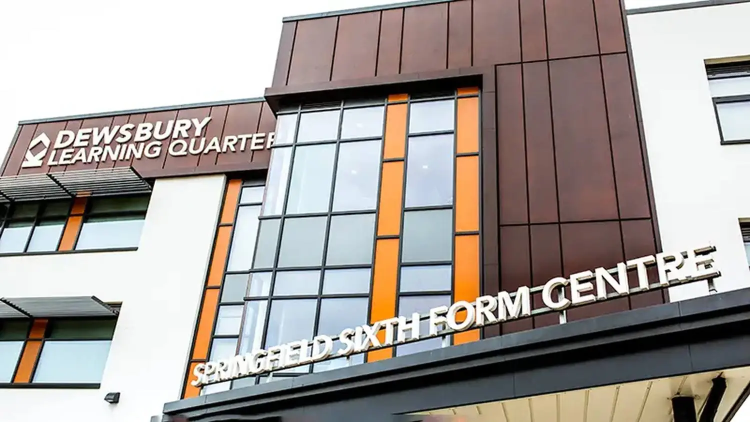 Modern college building with glass facade and signage. Students walking in front under a cloudy sky.
