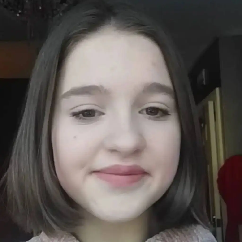 A young woman with short dark hair and a neutral expression poses for a close-up photo indoors.