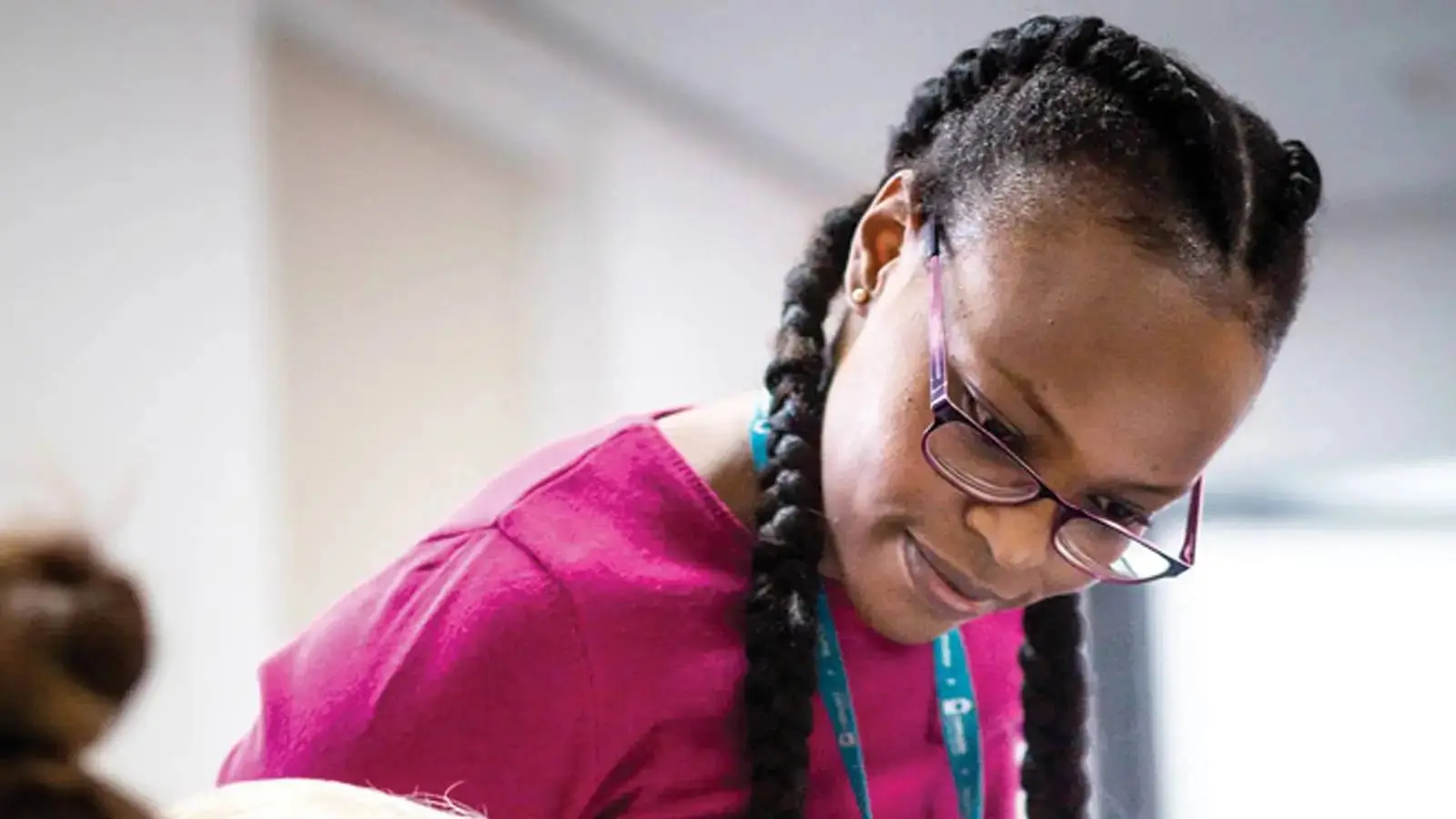A woman in a pink top and glasses looks down at a baby, possibly in a healthcare or educational setting.