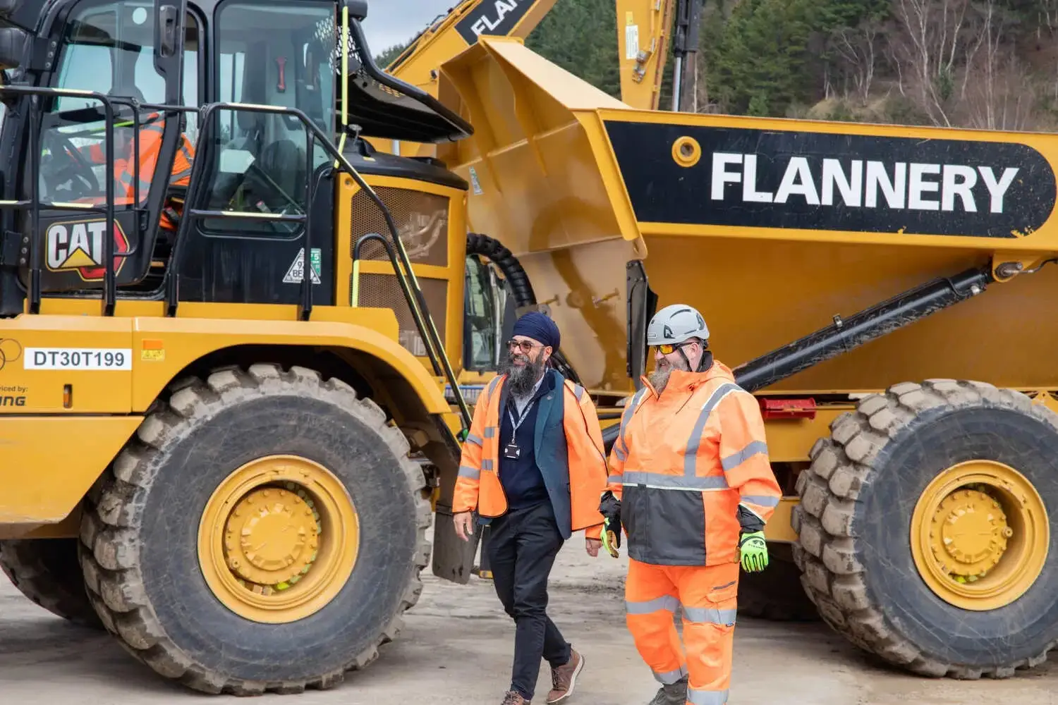 Two men in high-visibility clothing standing next to a large yellow construction vehicle with FLANNERY on the side.