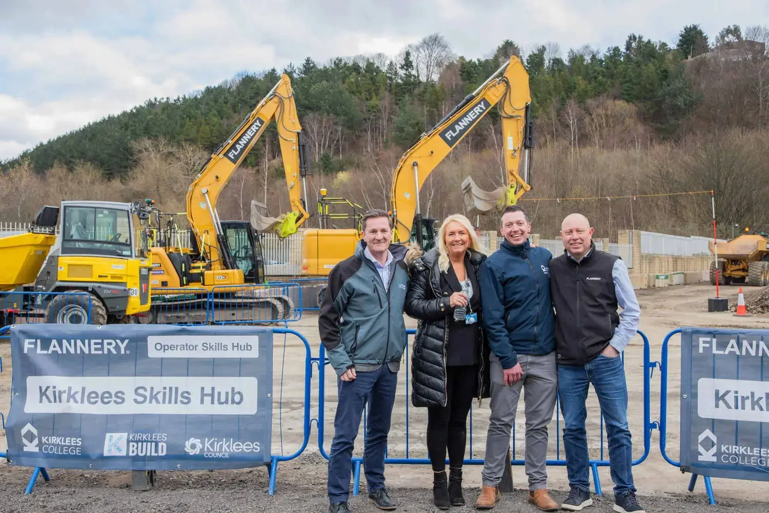 Four people standing in front of construction equipment and barriers labelled Kirklees
