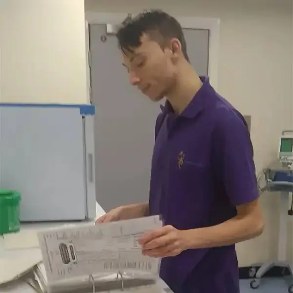 A student in a purple polo shirt reviews medical documents in a clinical setting, suggesting a focus on healthcare education.