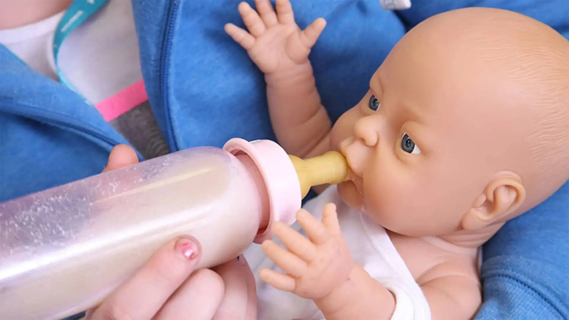 A doll being fed from a bottle by a person's hand, illustrating early childhood nutrition education.