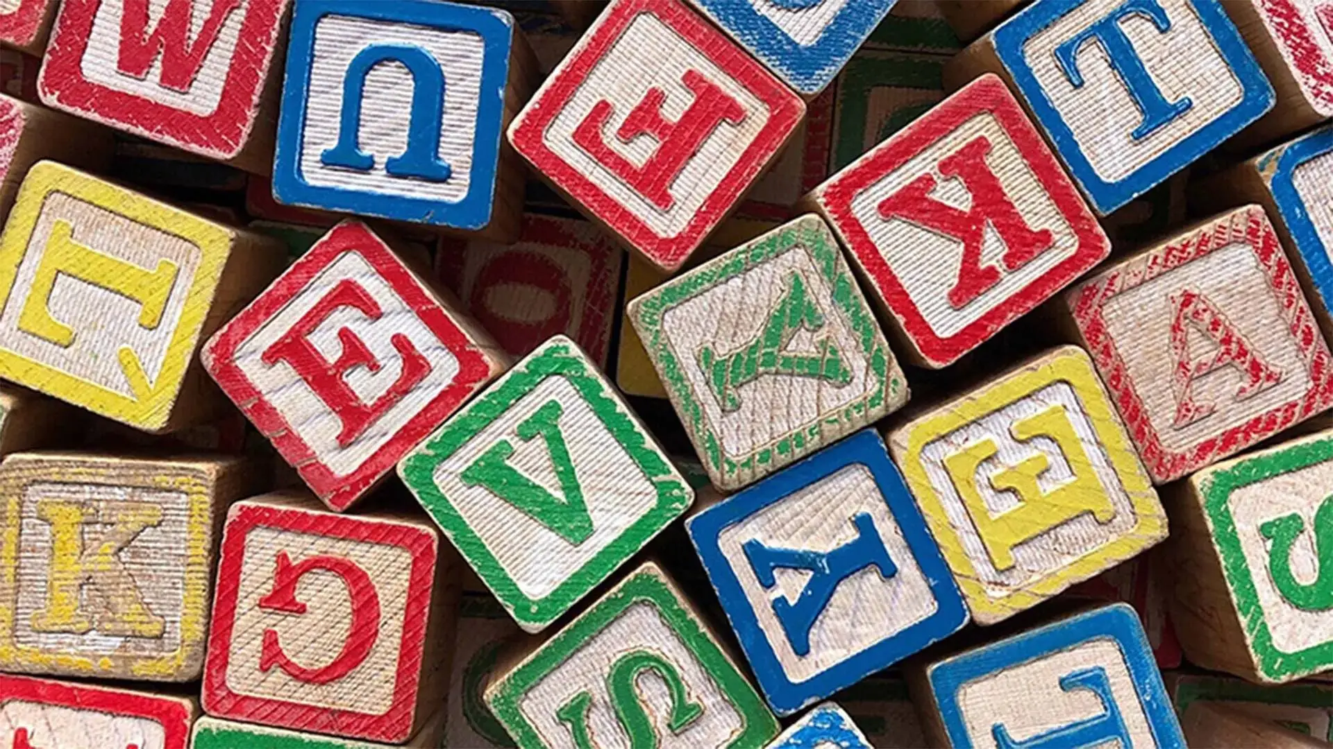 Colourful wooden alphabet blocks scattered, showcasing letters in red, blue, green, and yellow on a wooden surface. Ideal for early childhood education visuals.
