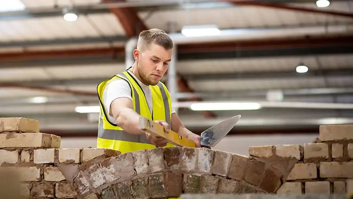 A man in a high-visibility vest laying bricks with a trowel in a construction setting.