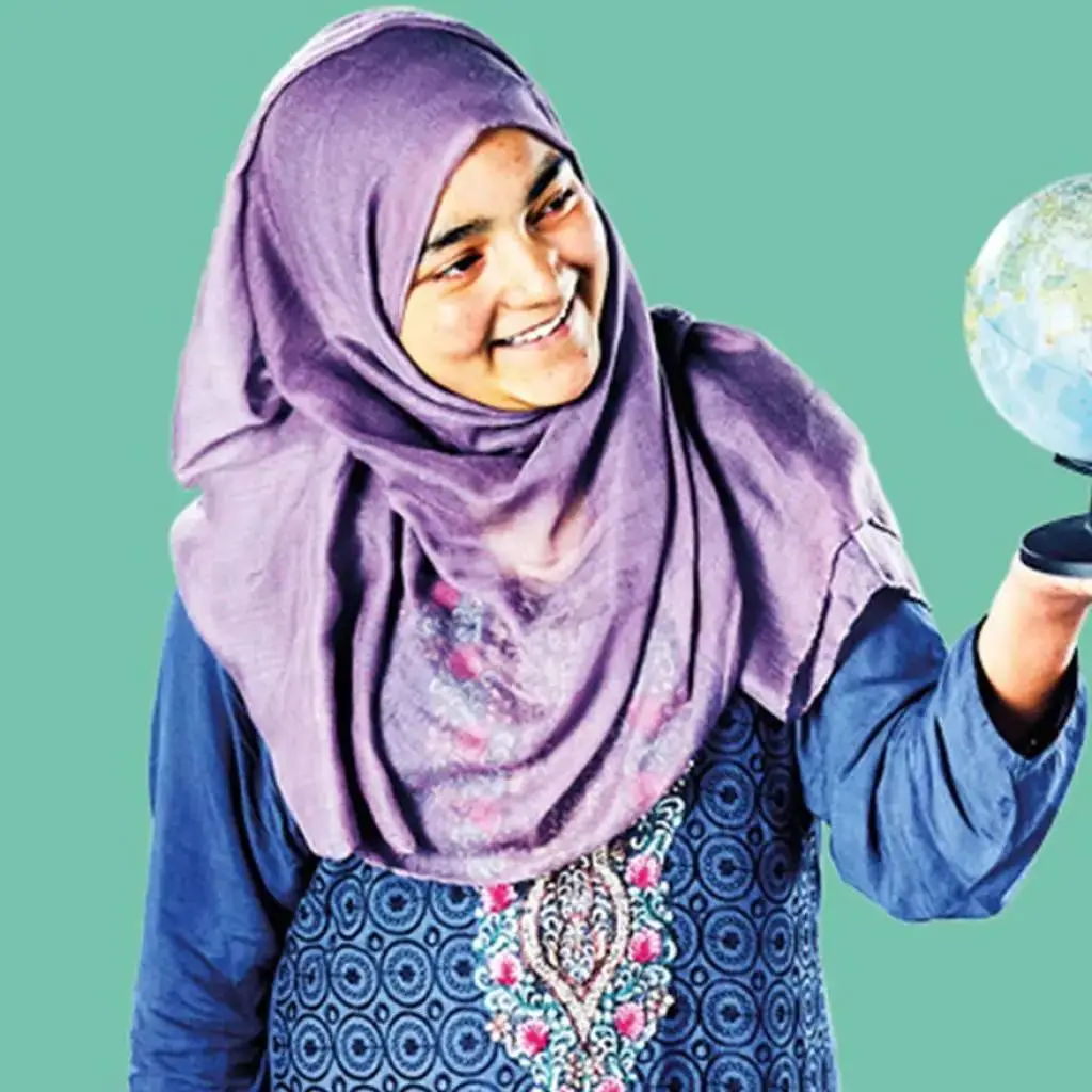 A woman in a purple headscarf smiling and holding a globe against a green background.
