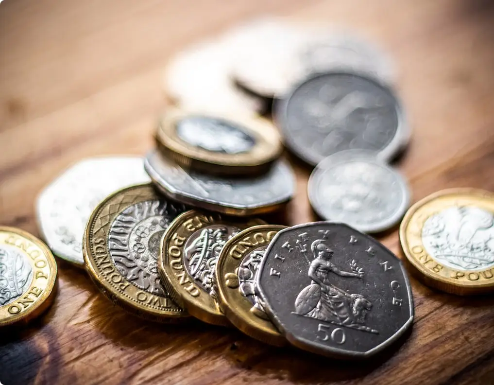 A pile of British coins, including 50p, £1, and 2p, on a wooden surface. Educational focus on currency design and history.