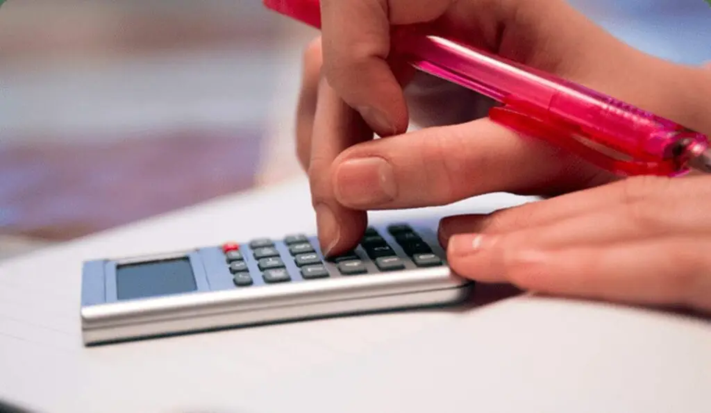 A person using a calculator and pen on a white surface, likely engaged in mathematical calculations or problem-solving.