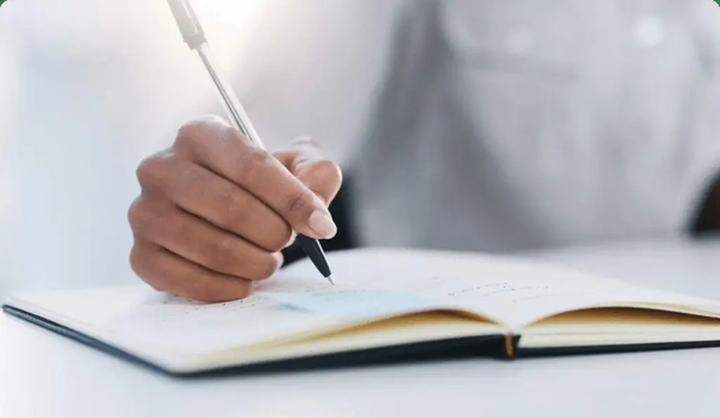 A person writing in a notebook with a pen, focused on their studies.