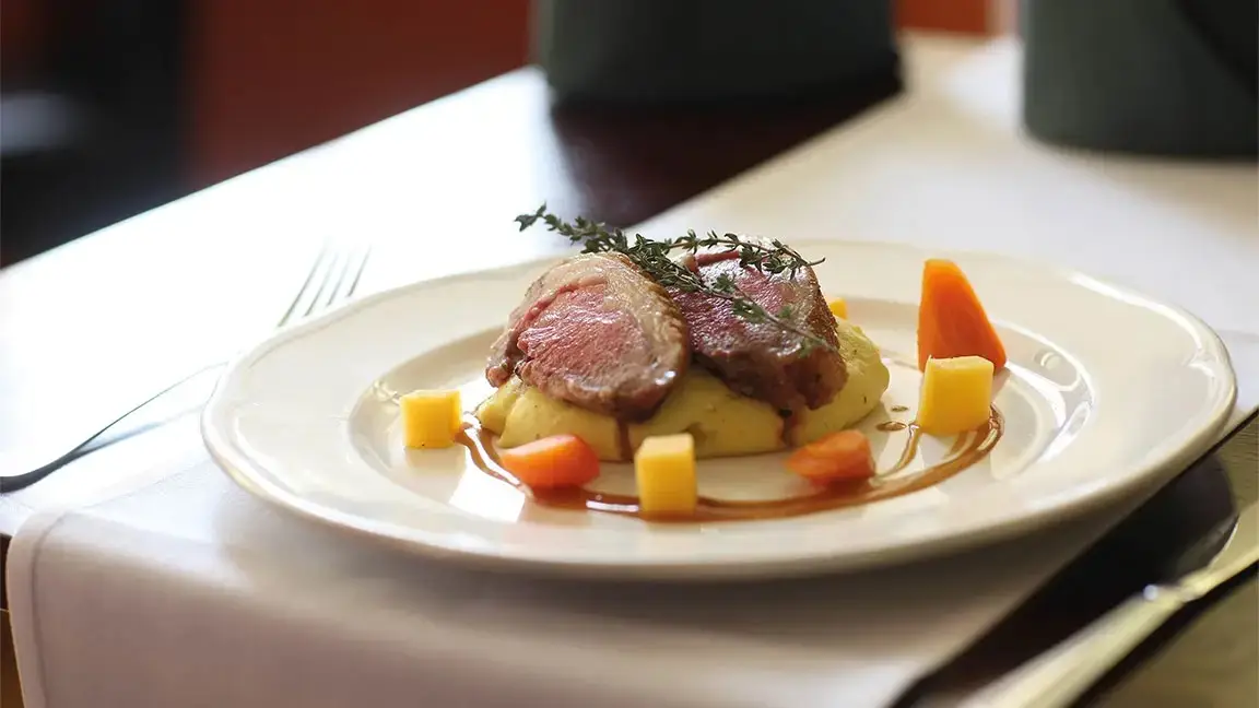 A plate of lamb chops on mashed potatoes with carrots and a brown sauce.