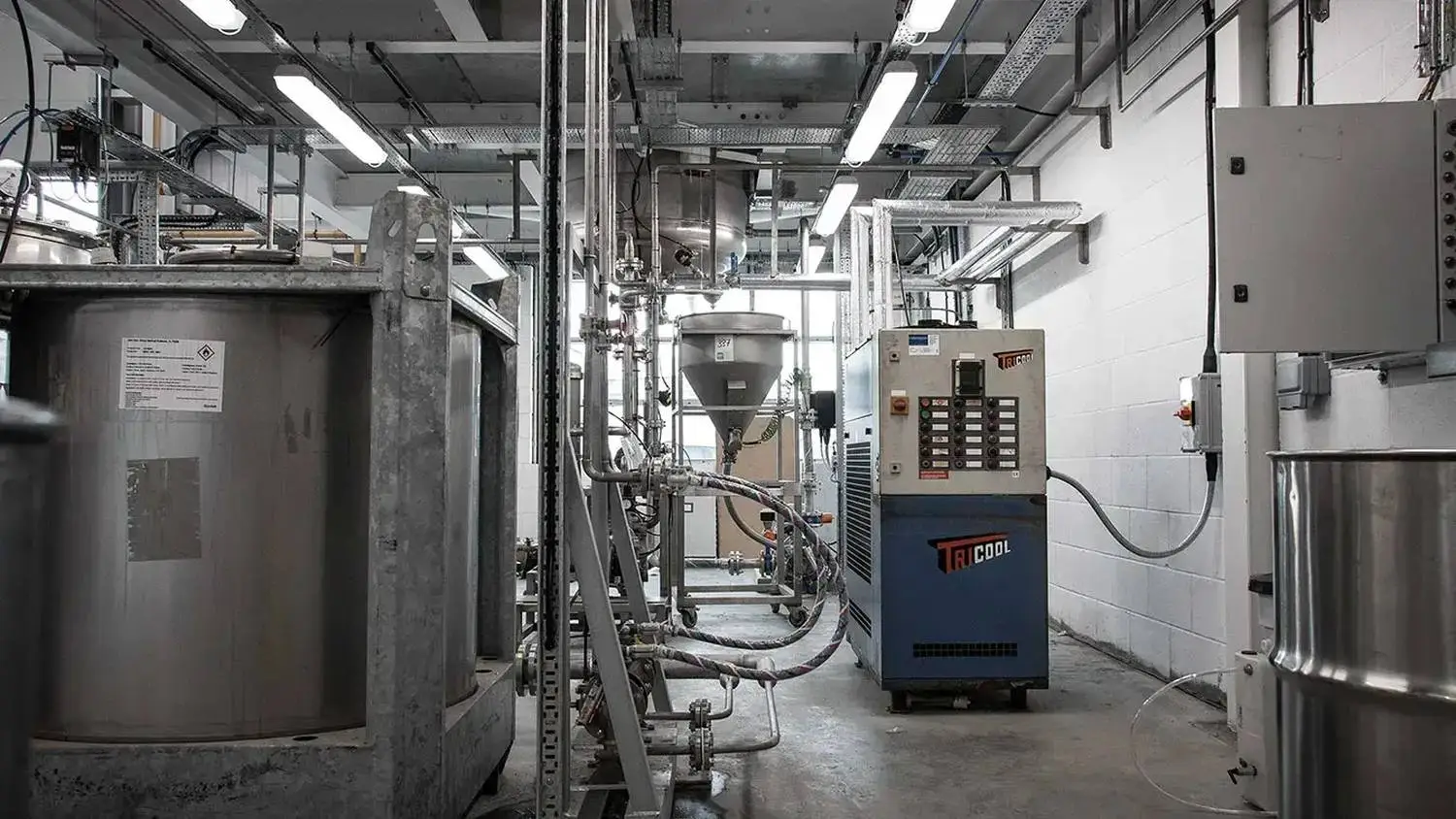 Industrial laboratory with stainless steel tanks, pipes, and control panels. Bright overhead lighting illuminates the clean, organised space, ideal for scientific research and experimentation.