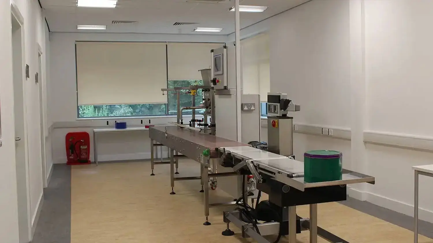 A clean, well-lit room with a conveyor belt, industrial equipment, and a window, likely used for food processing or manufacturing training in a UK college.