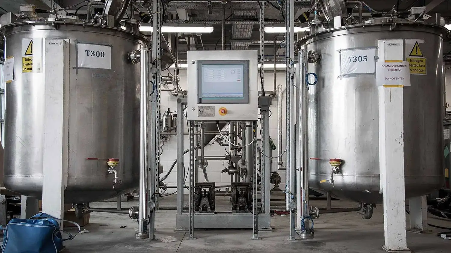 Two large stainless steel tanks with a control panel in between, labelled T300 and T305, in an industrial setting.