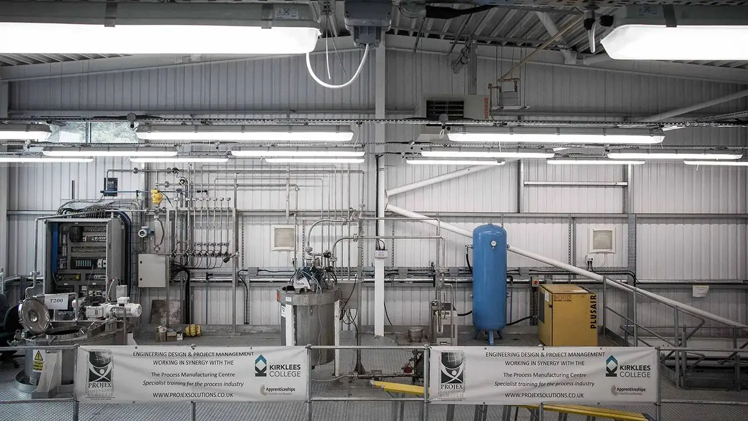 Industrial facility with machinery and pipes, banners promoting engineering and project management courses at ProjeX Solutions College.