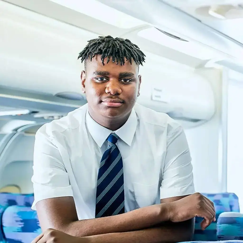 A young man in a white shirt and striped tie sits confidently in a train carriage, suggesting a journey towards academic success.