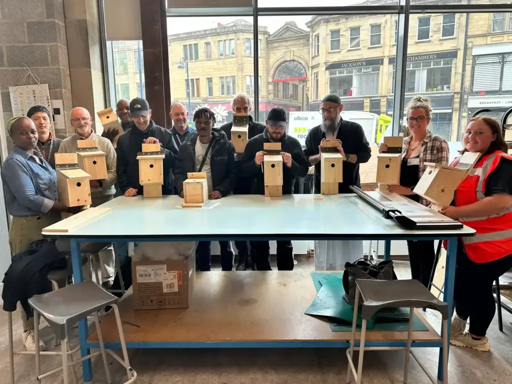 Group of people stand around a table in front of window holding bird boxes.