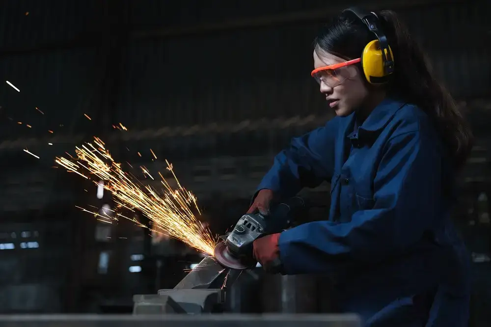 Female metal worker using industrial machinery in manufacturing factory with sparks
