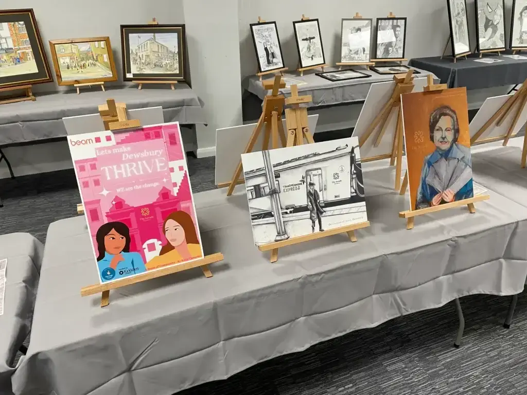 Three artworks on easels on top of table with grey tablecloth