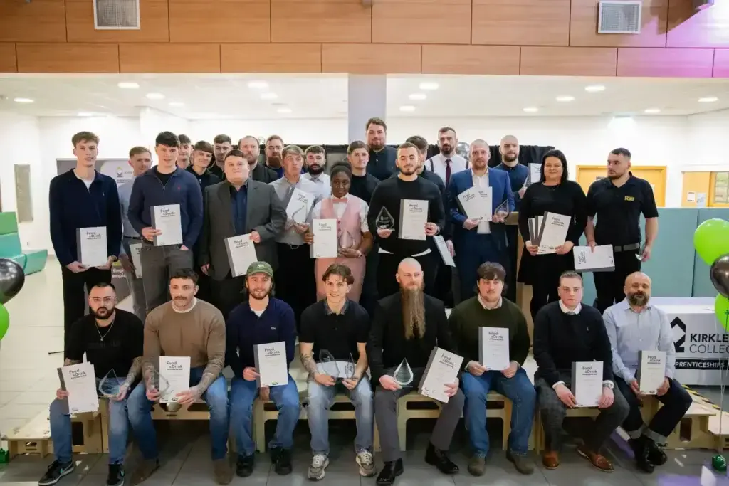 Two rows of students stand on stage holding certificates