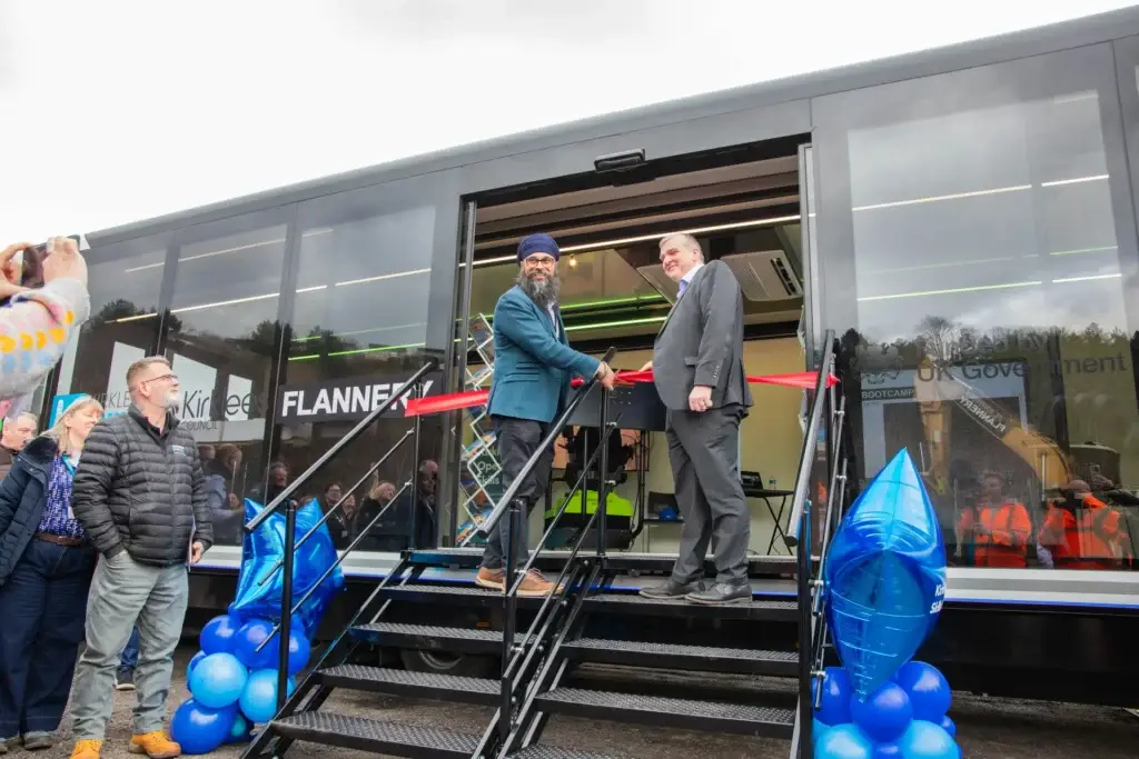 two men standing either side of a pair of scissors cutting a ribbon