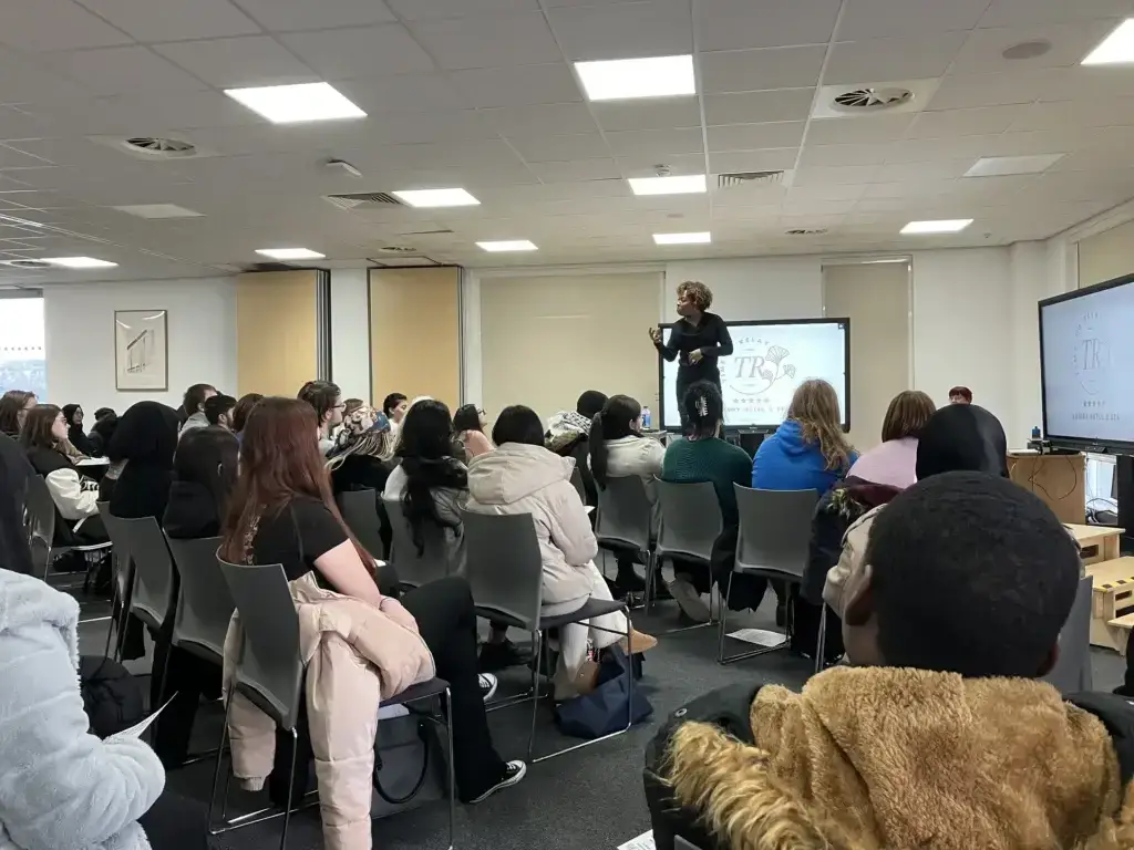 Woman stands on stage giving a speech to students in a conference room