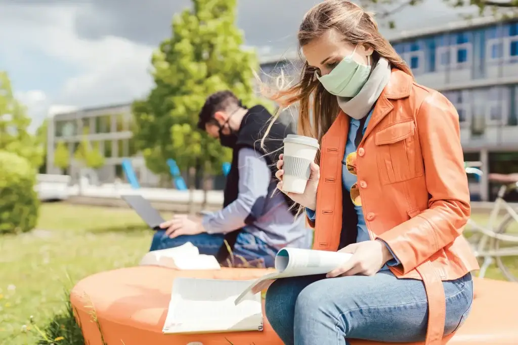 Woman sat with coffee cup on a bench with a mask on