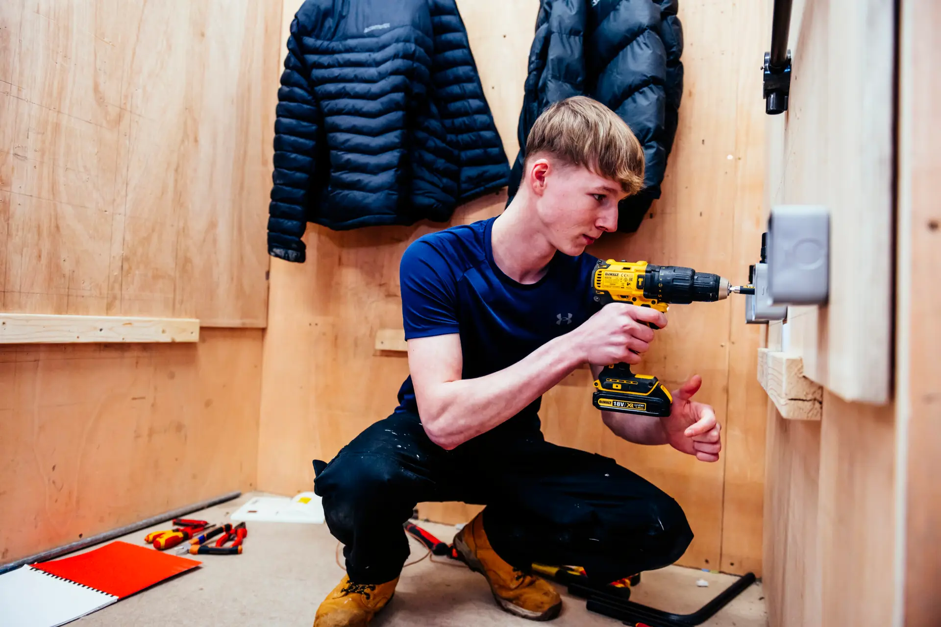 Student kneels in electrical bay using drill