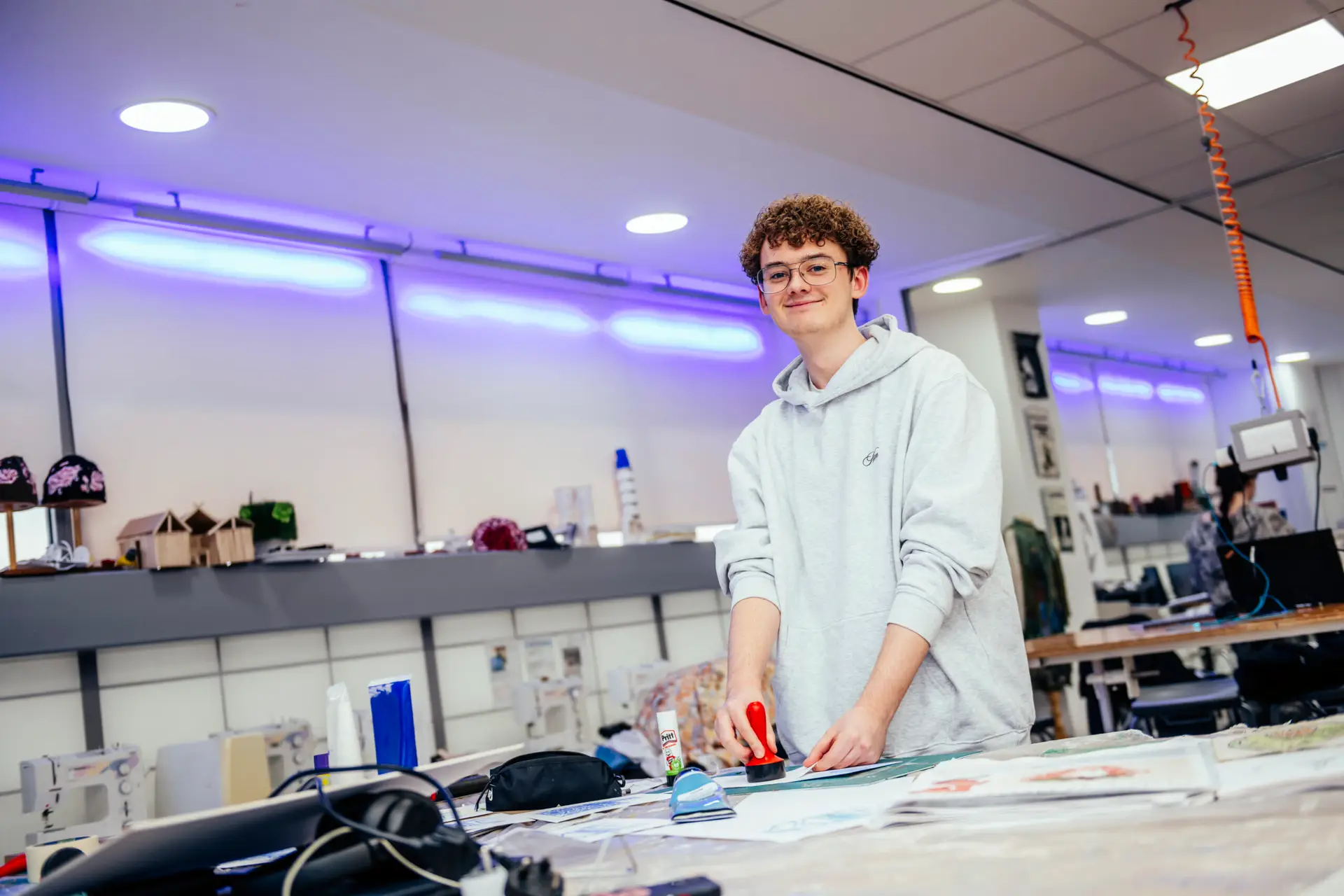 male student stands at art desk using a small printing block