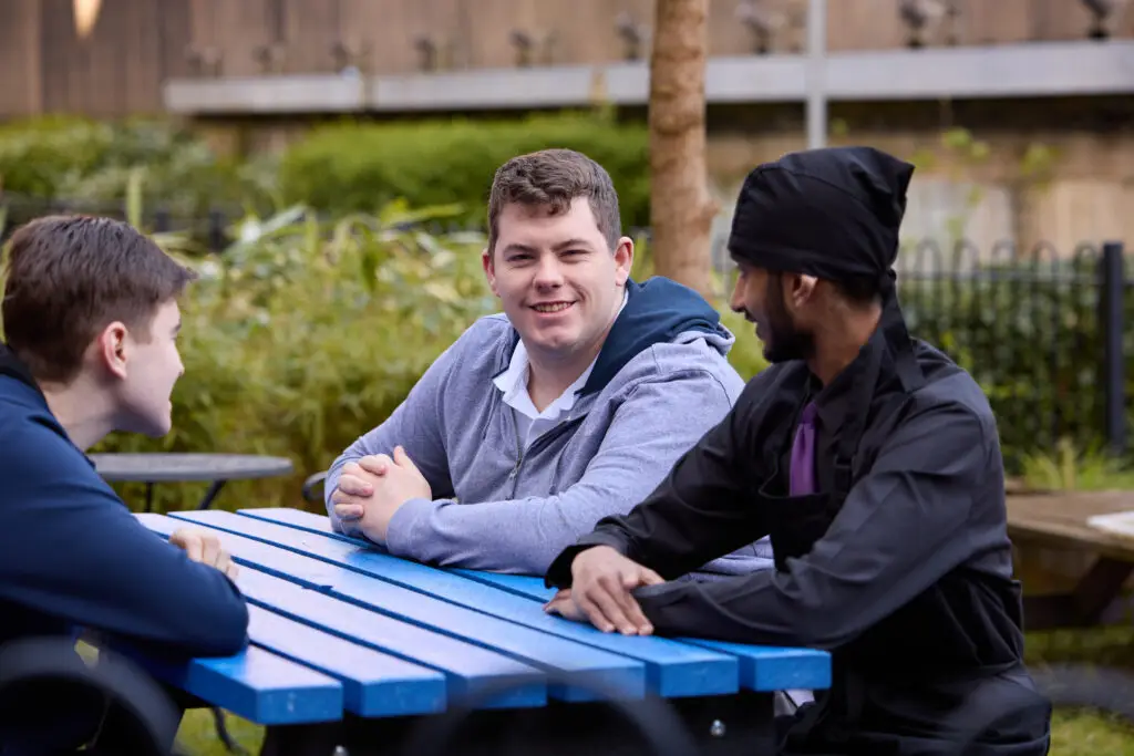 Three young men sit around a table chatting