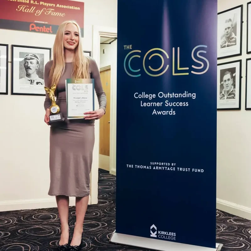 A woman in a grey dress holding a certificate and trophy next to a blue banner for the College Outstanding Learner Success Awards.