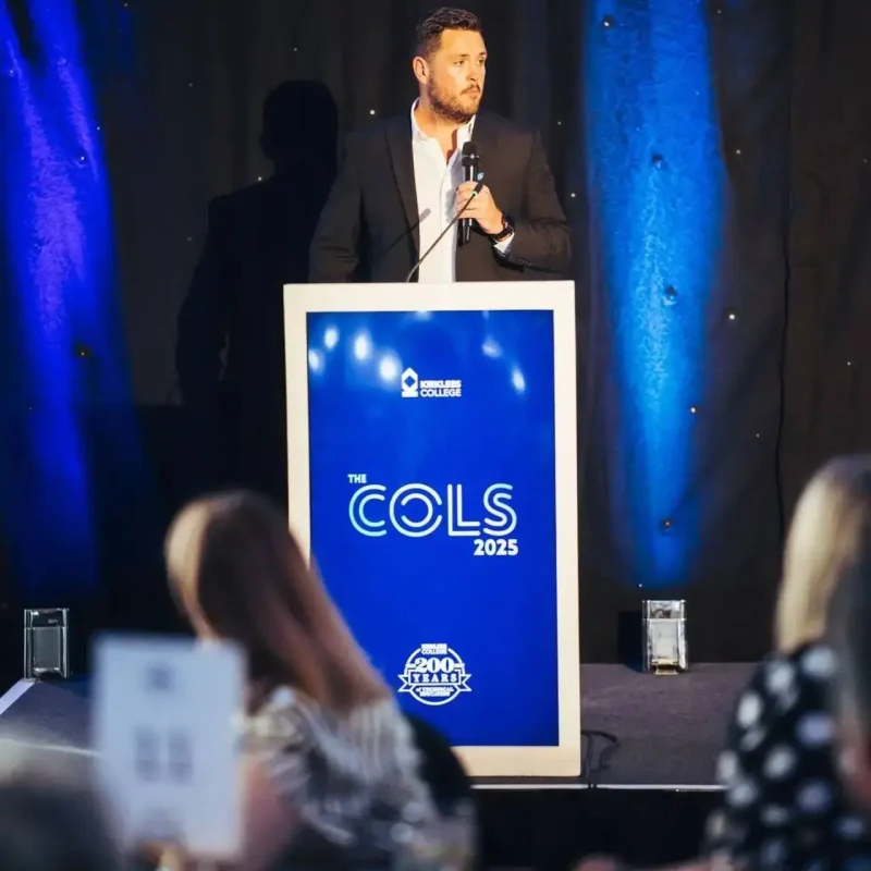 A man in a suit speaking at a podium with The