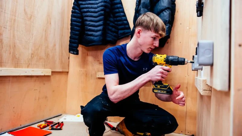 Student kneels in electrical bay using drill