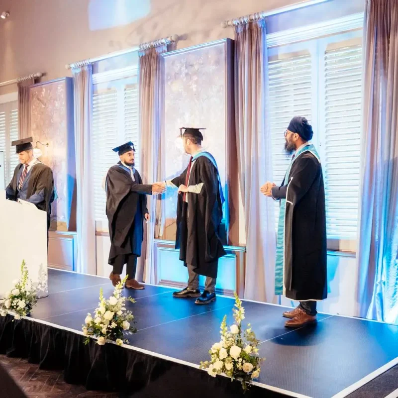 Graduation ceremony on stage with cap and gown, flowers, and a podium. Academic achievement celebrated in a formal setting.