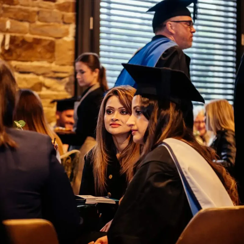 Graduates in caps and gowns seated at a ceremony, receiving certificates from faculty in academic regalia.